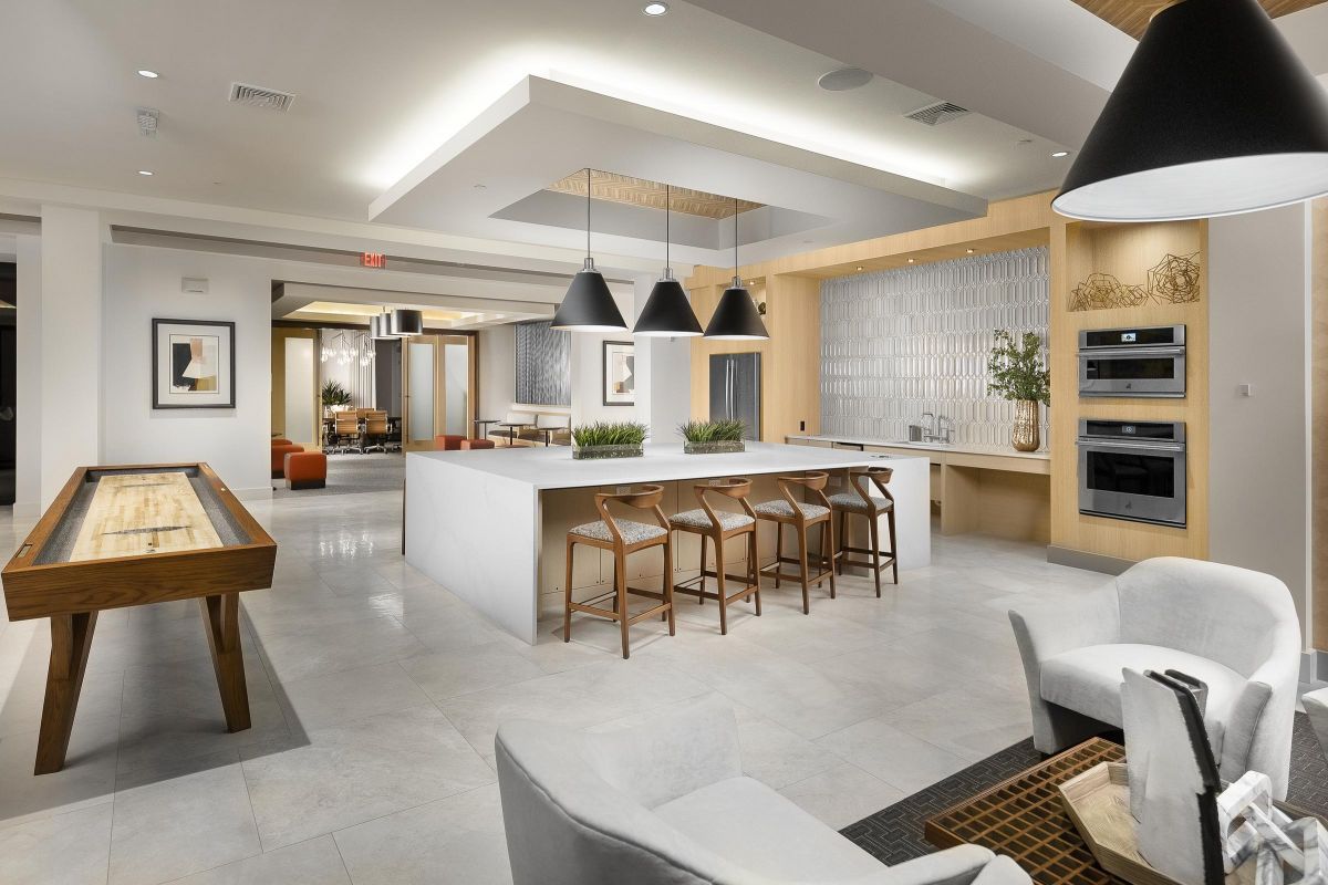 Modern lounge with a kitchen island, bar stools, shuffleboard table, and elegant lighting.