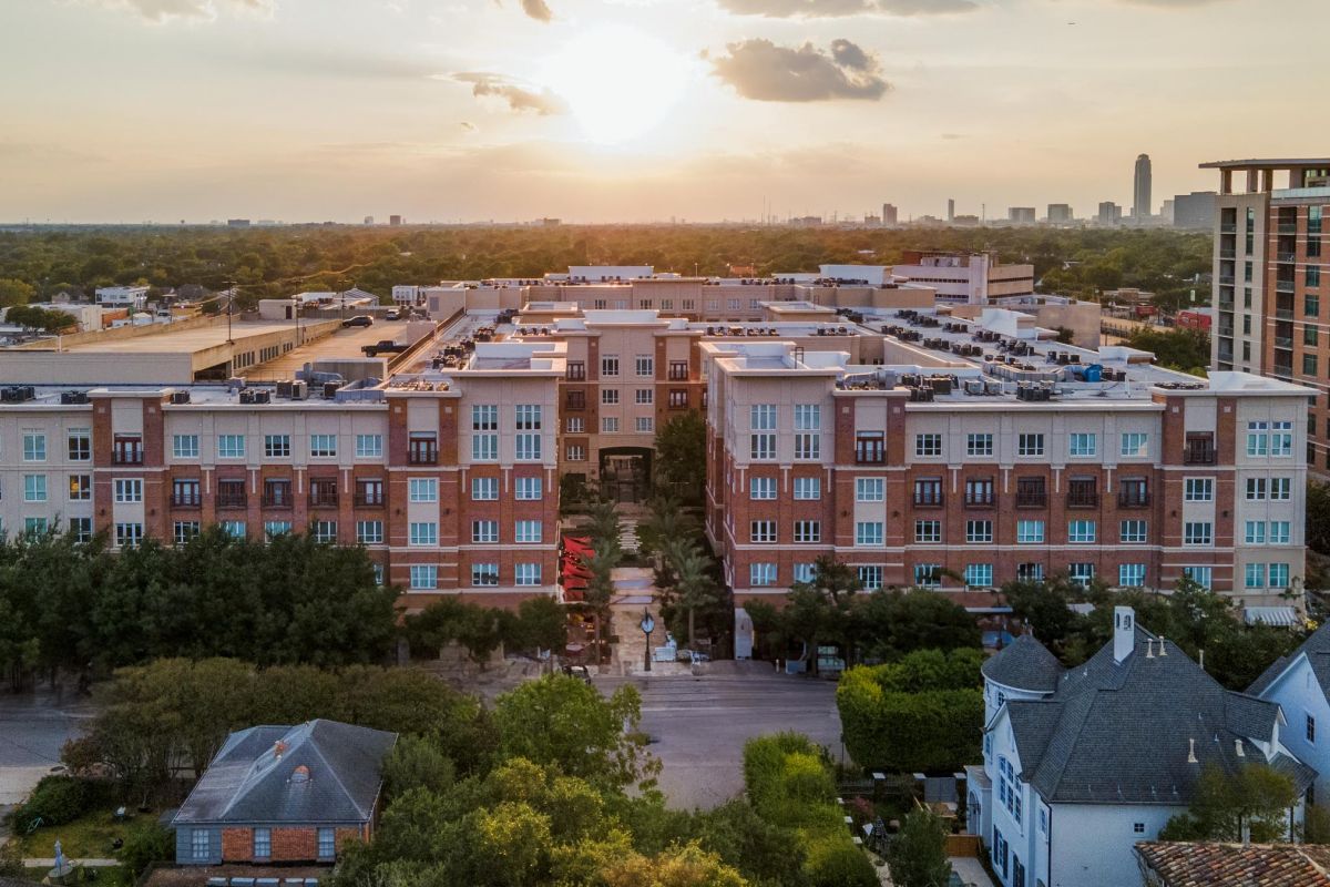 Hanover Company Aerial view of a residential complex at sunset, with trees and buildings in the foreground and city skyline in the distance.