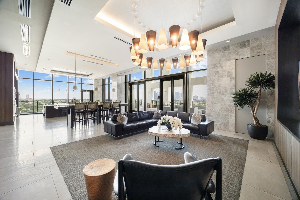 Modern lounge with large windows, black sofas, bar area, and a view of the city skyline.
