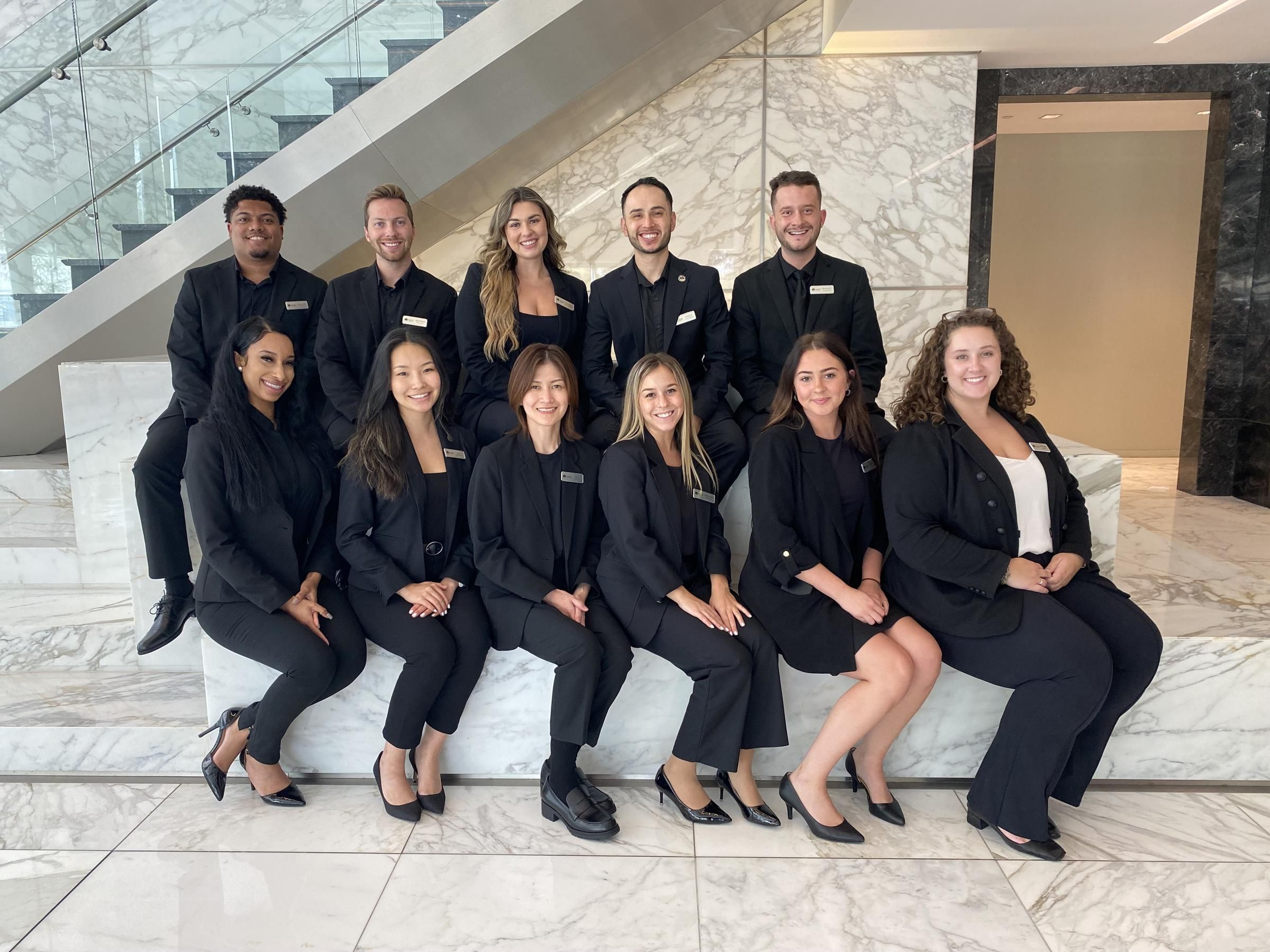 Hanover Company group of eleven people in black professional attire sitting and standing on marble steps indoors.