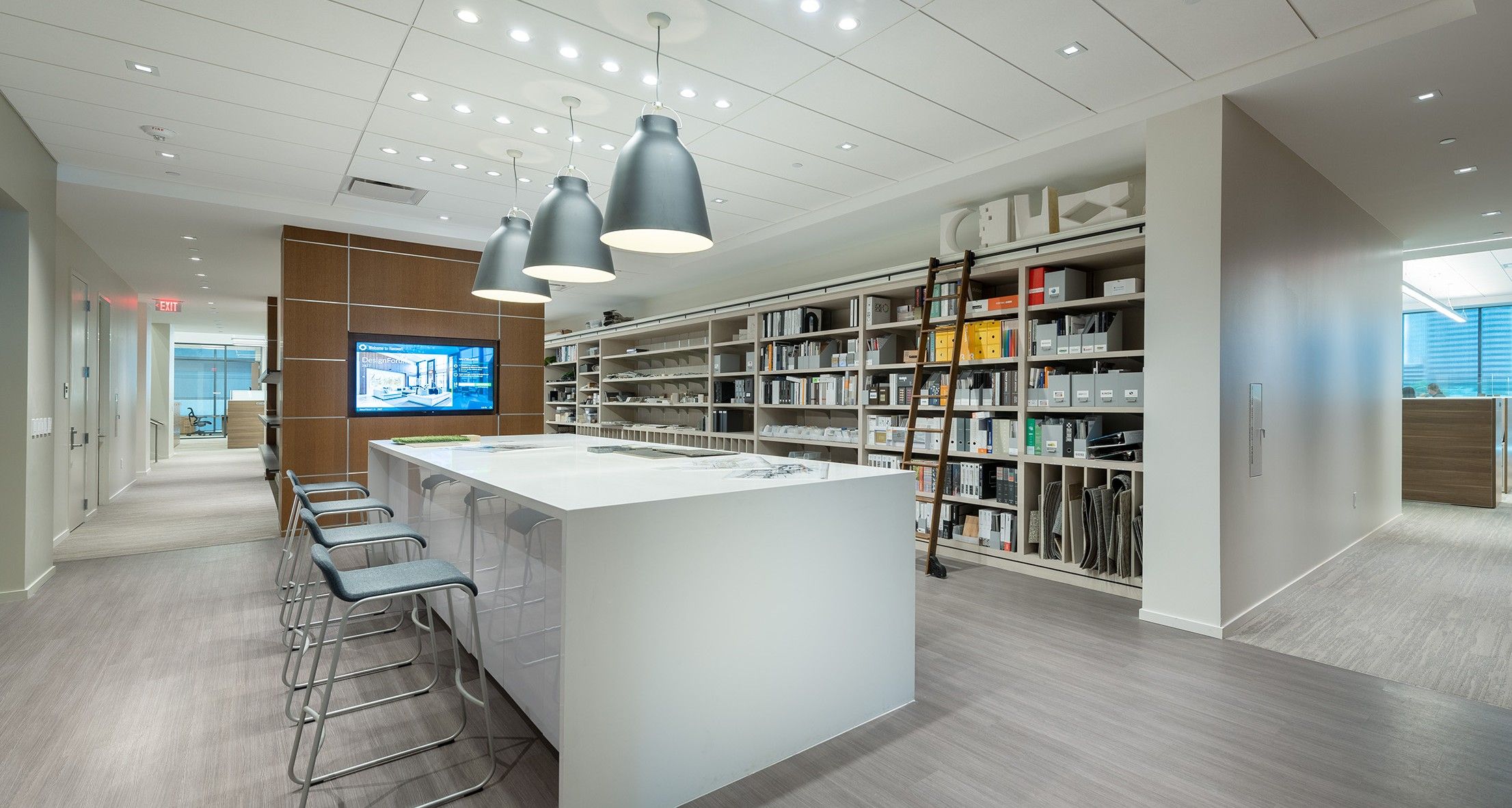 Modern office at Hanover Company interior with a large table, barstools, shelves of materials, and a wall-mounted screen.