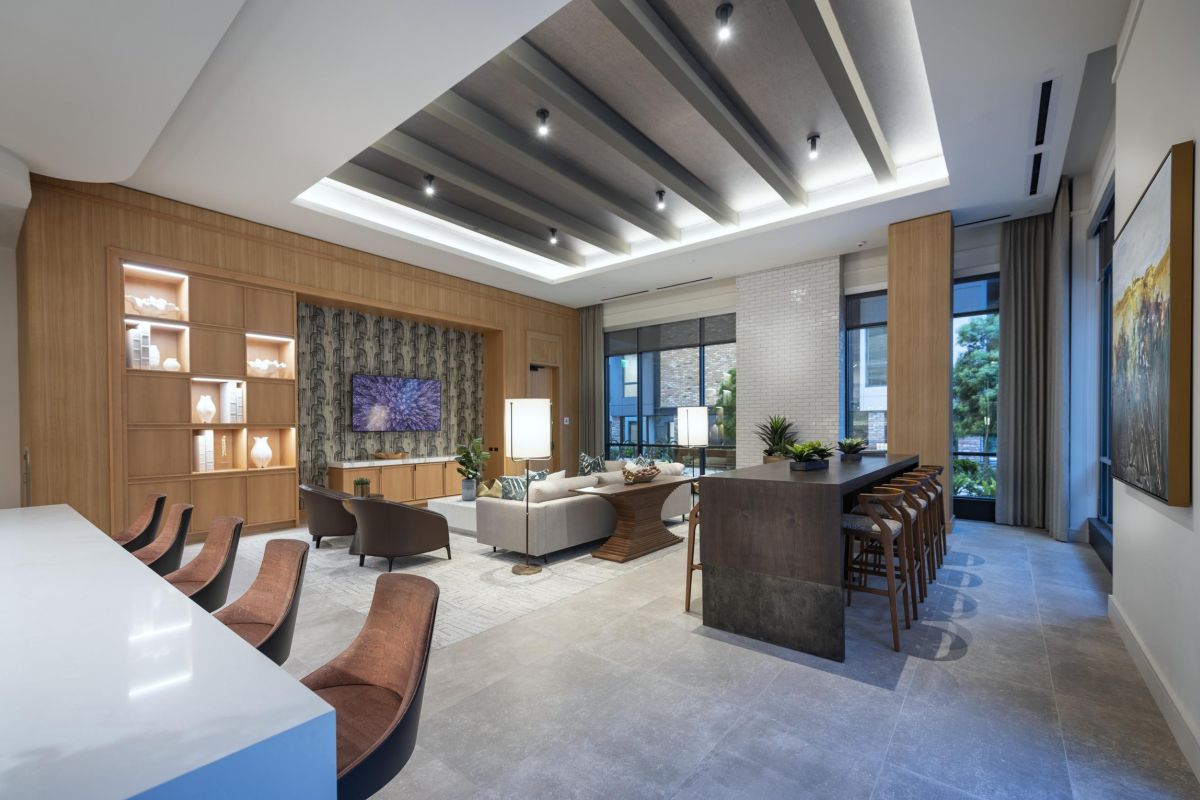 Modern living room with a large sofa, wall-mounted TV, bar with stools, and decorative shelving under a coffered ceiling.
