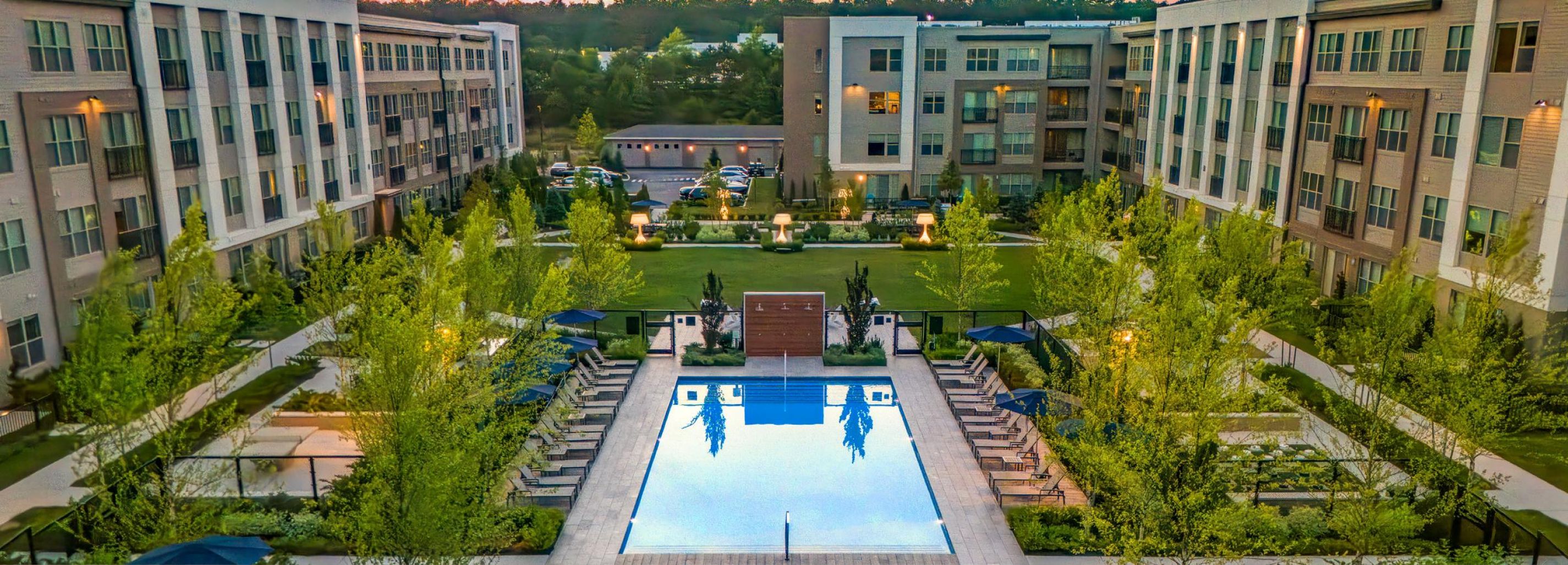 Aerial view of a modern apartment complex with a central courtyard featuring a pool, surrounded by trees and buildings.