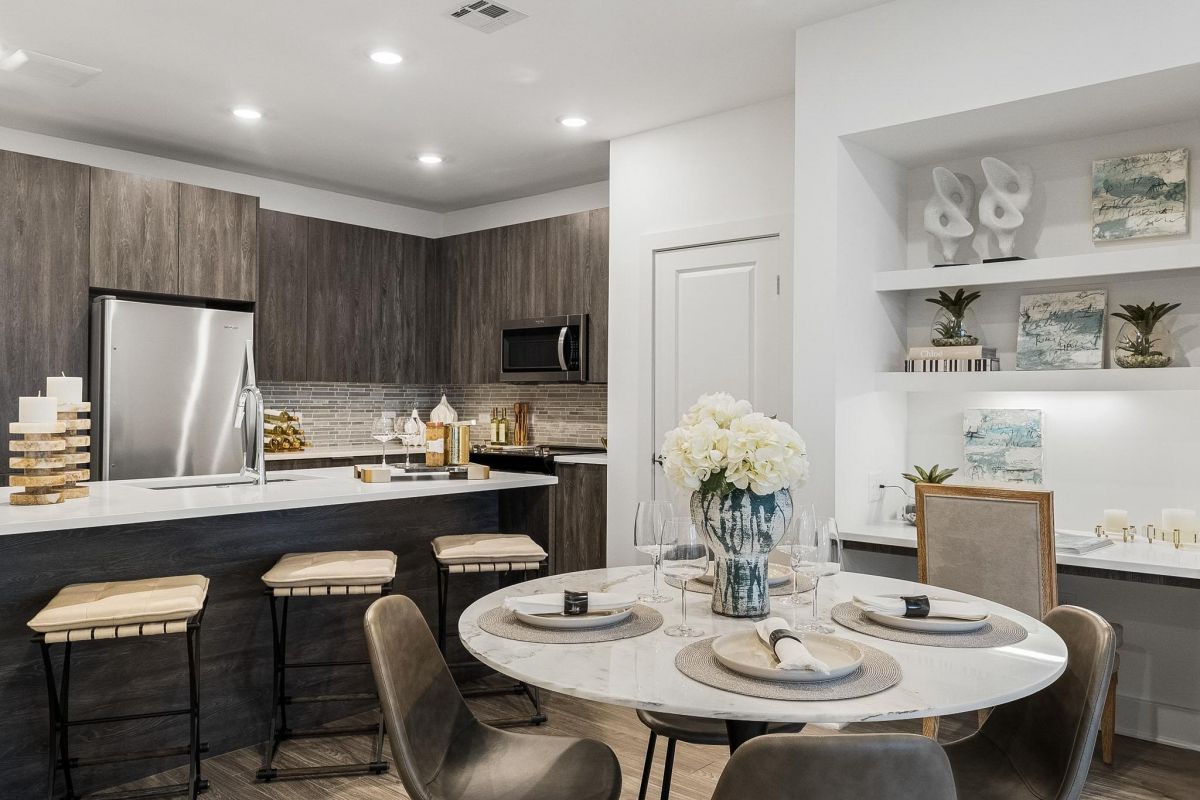 Modern kitchen with dark wood cabinets, bar stools, and a round dining table set with flowers and elegant decor.