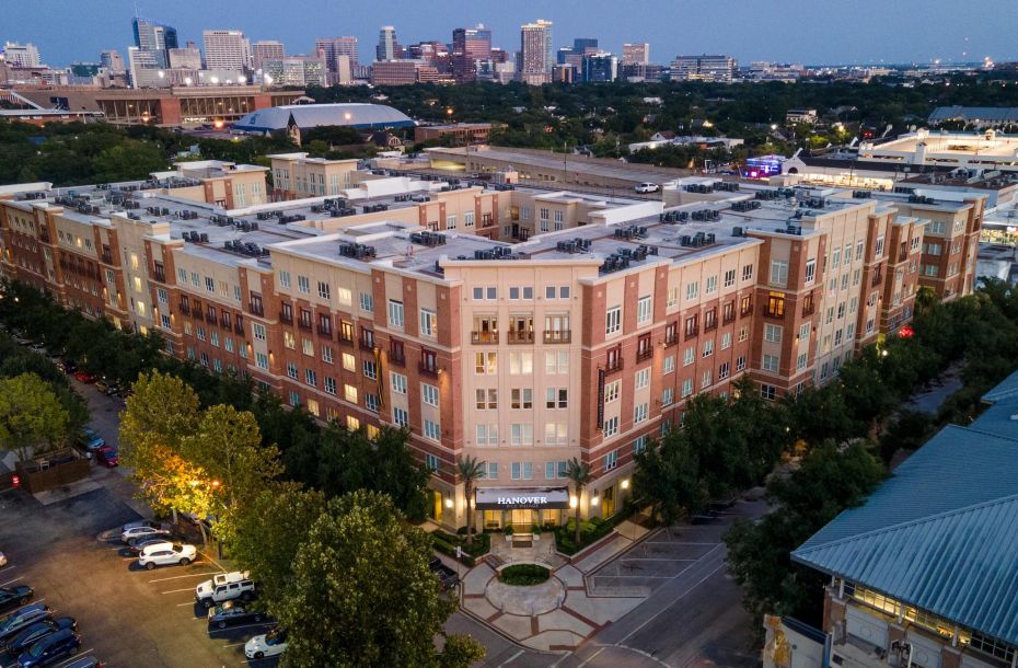 Hanover Company Aerial view of a large apartment complex with cityscape background at dusk.