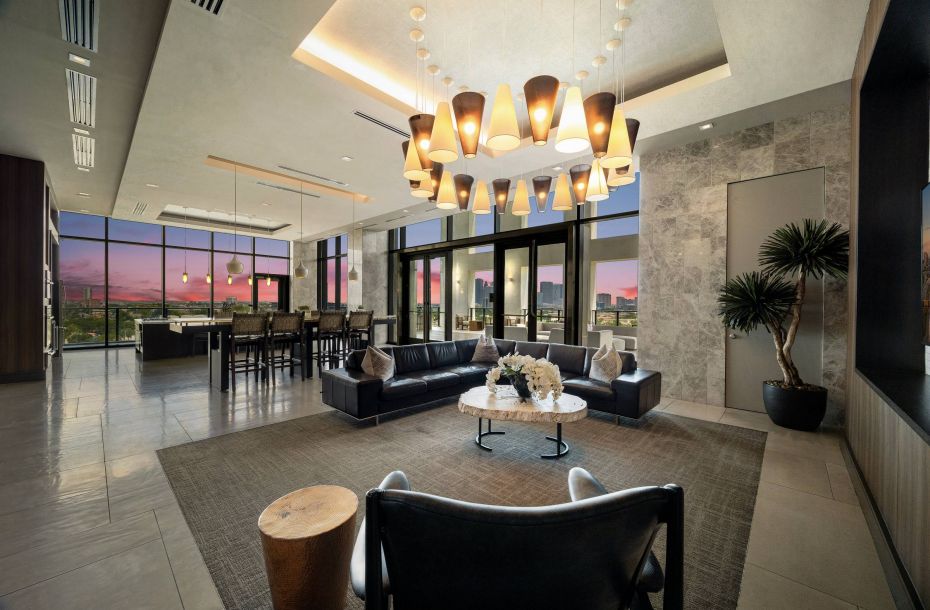 Hanover Company, Hanover Montrose Luxurious modern lounge with leather sofas, a large chandelier, and floor-to-ceiling windows showing a city skyline at sunset.