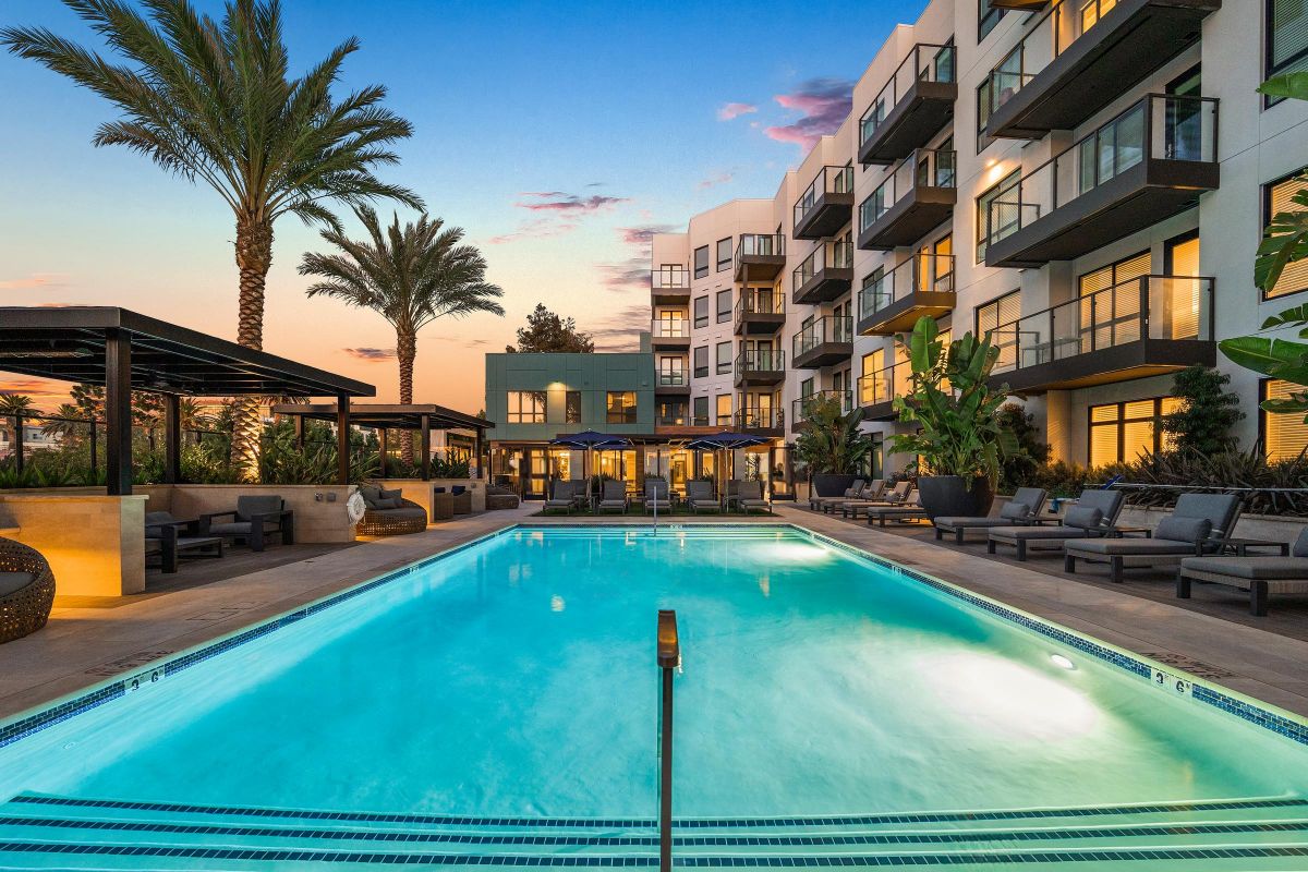 Luxurious pool area at sunset, surrounded by palm trees and modern apartment building with balconies.