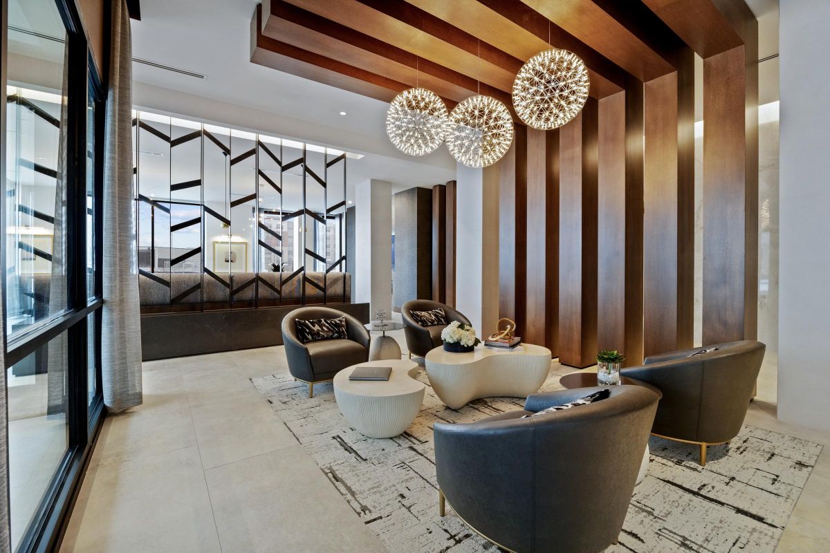 Modern lounge with geometric wood panels, round chandeliers, gray chairs, and abstract wall art. Light, airy space.