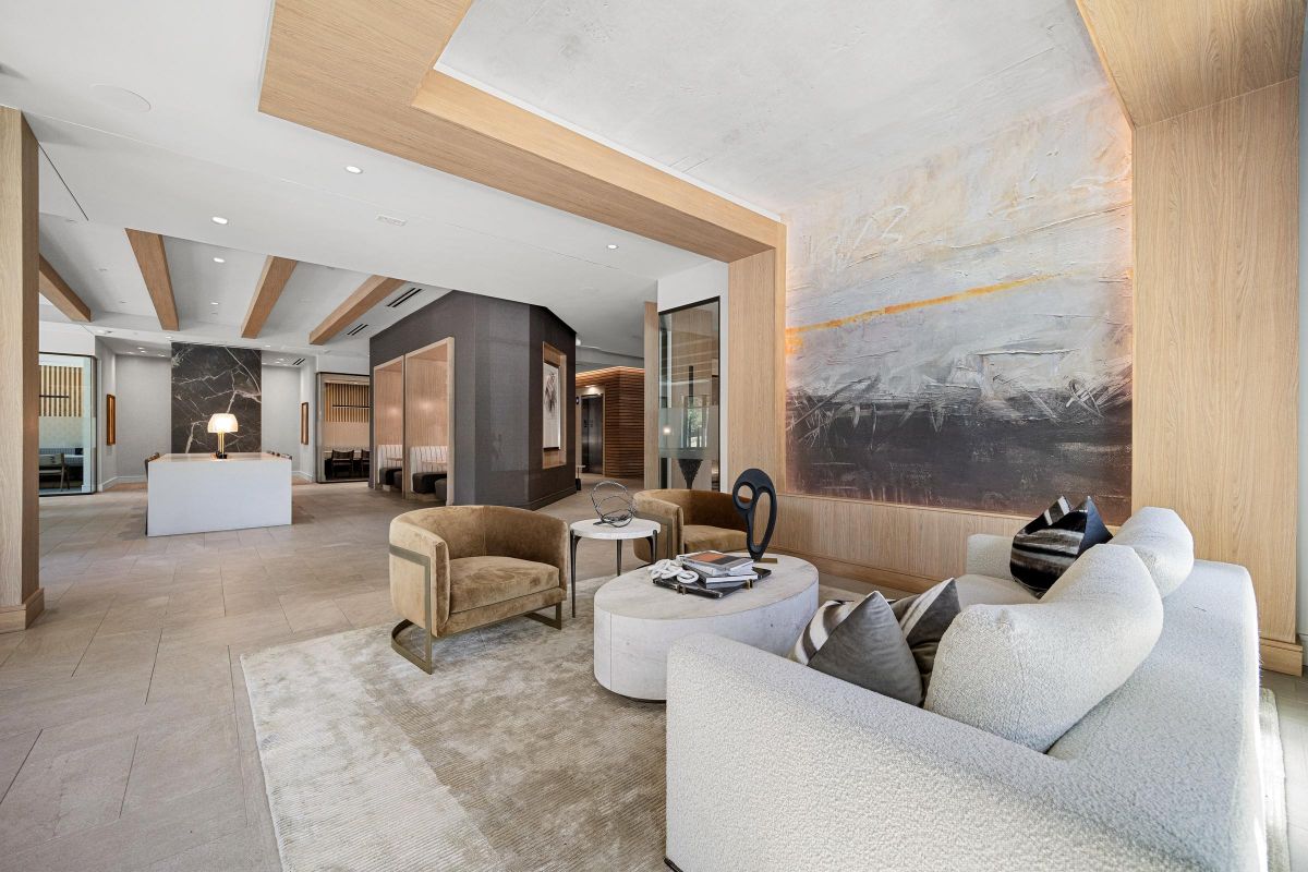 Modern lounge with beige sofas, armchairs, abstract wall art, and decorative items on a round coffee table.