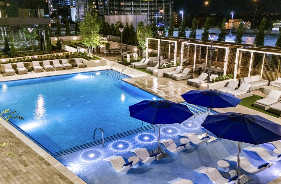 Hanover Company, Hanover Midtown Luxurious outdoor pool area at night with lounge chairs, umbrellas, and ambient lighting.