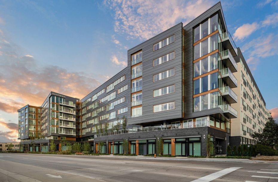 Hanover Company, Hanover RiNo Modern multi-story apartment building with large windows, balconies, and sunset sky in the background.