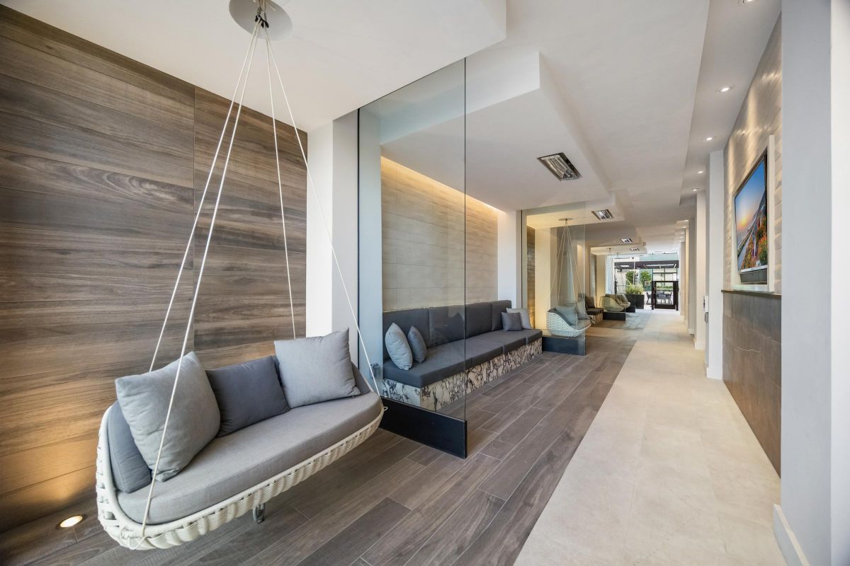 Modern hallway with wooden and glass walls, featuring a hanging wicker chair and cushioned benches.