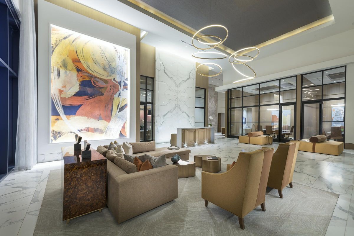 Modern lobby with abstract art, circular lights, beige seating, marble floor, and natural lighting.