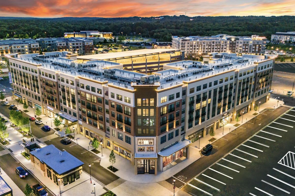 Aerial view of a modern apartment complex with surrounding parking lots at sunset.