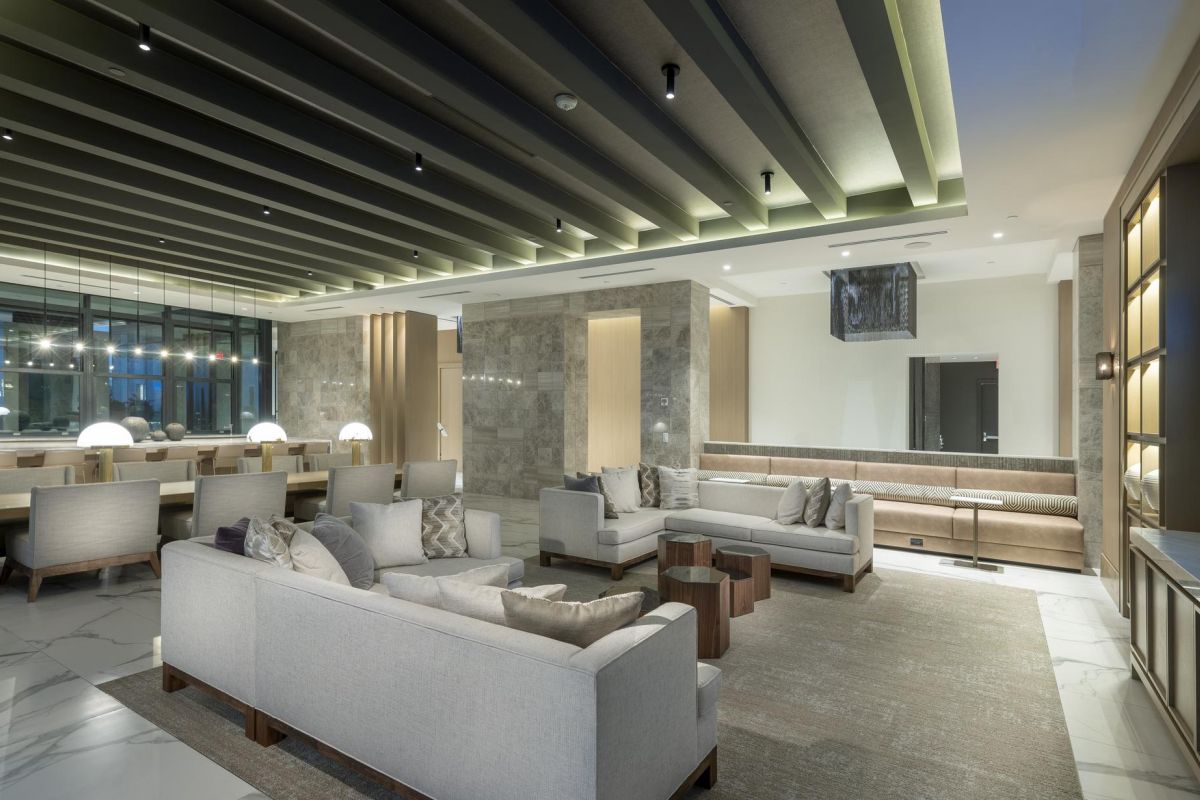 Modern lounge with sofas, a large dining table, and a wall-mounted TV, featuring soft lighting and marble flooring.