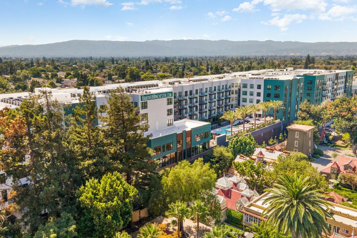 Aerial view of a modern apartment building surrounded by trees, with mountains in the background.