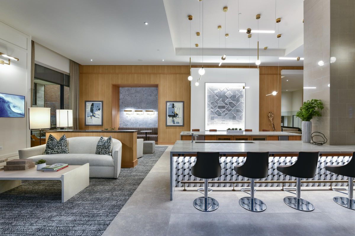 Modern lounge with a sofa, bar stools, contemporary lighting, art on walls, and wood-paneled accents.