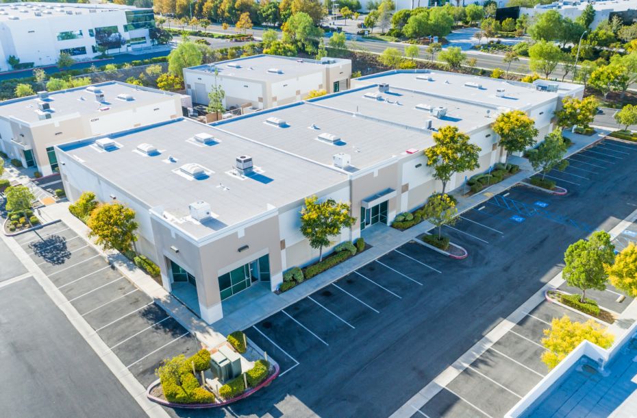 Aerial view of a modern business park with empty parking lots and surrounding trees.