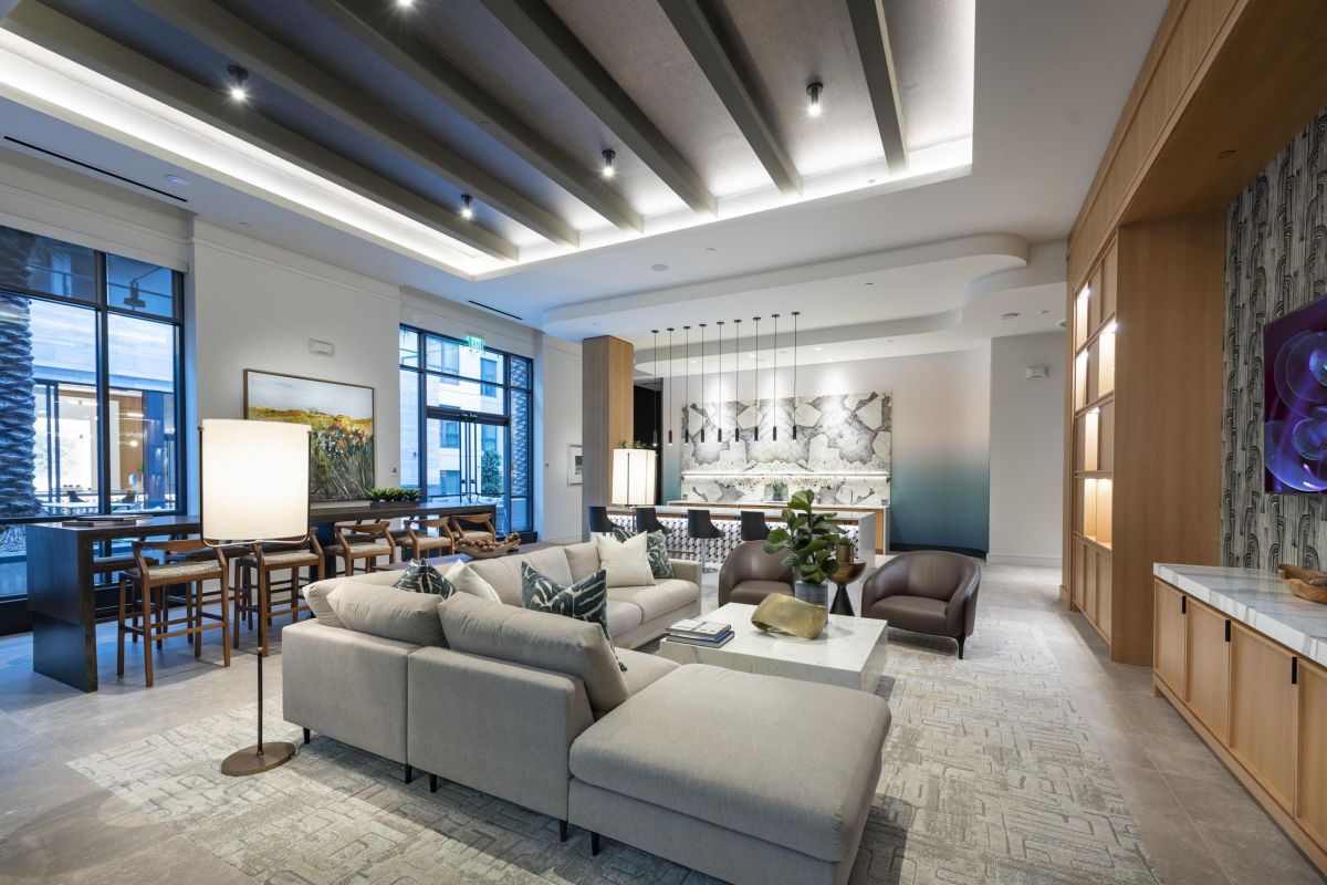 Modern living room with a sectional sofa, armchairs, dining area, artistic wall decor, and large windows.