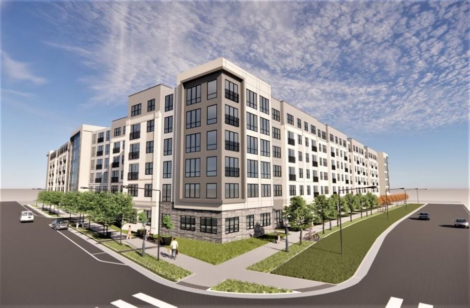 Modern multi-story apartment building with large windows and a landscaped sidewalk under a blue sky.