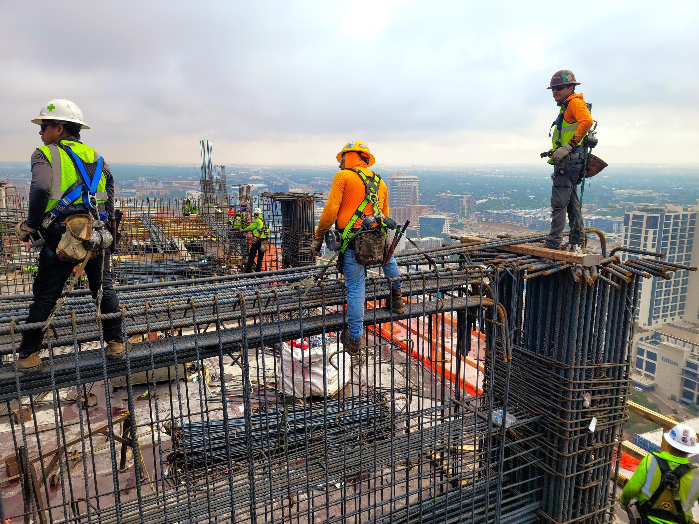 Construction workers in safety gear working on a high-rise building with cityscape in the background.