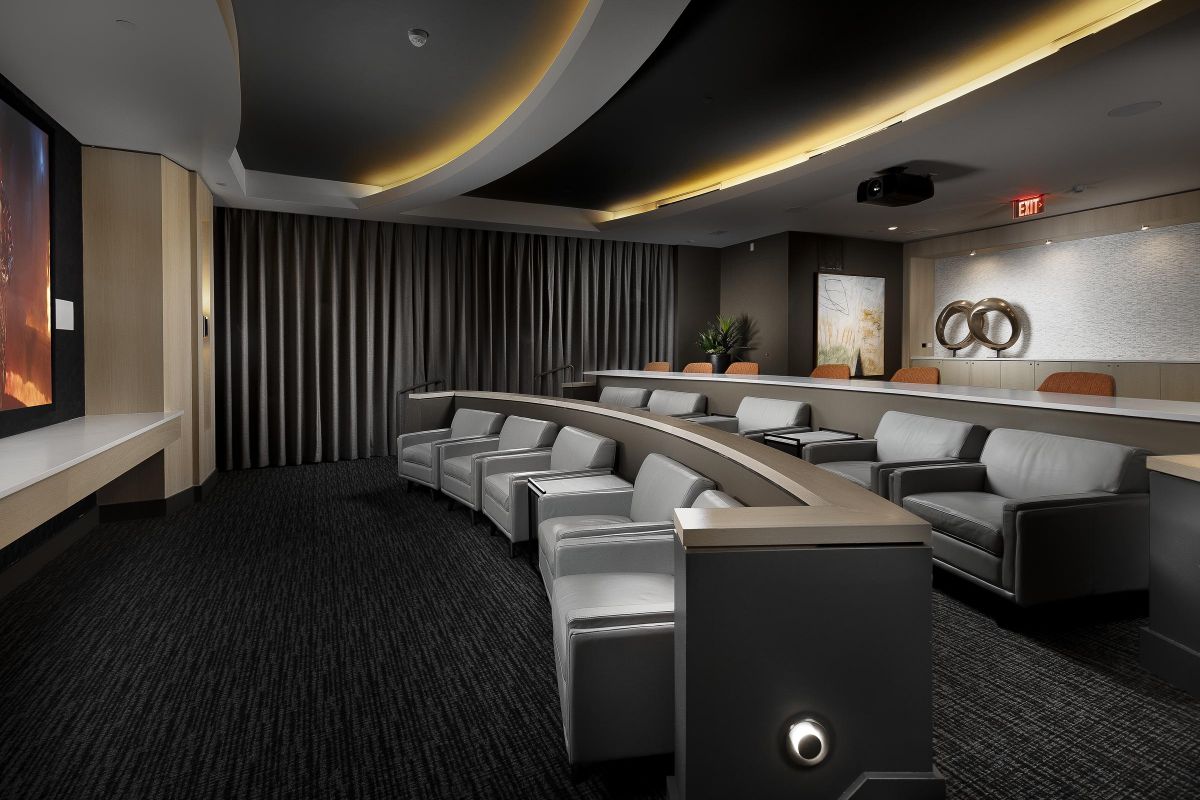 Luxurious home theater with gray seating, curved design, and dim lighting, featuring a large screen and modern decor.
