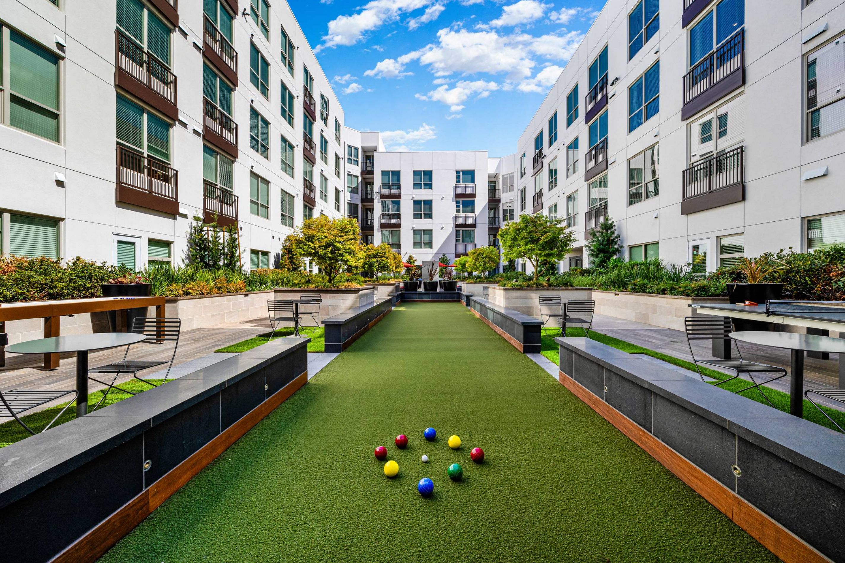 Hanover Company, Hanover Walnut Creek Courtyard with a bocce ball court, surrounded by modern apartment buildings and greenery under a blue sky.