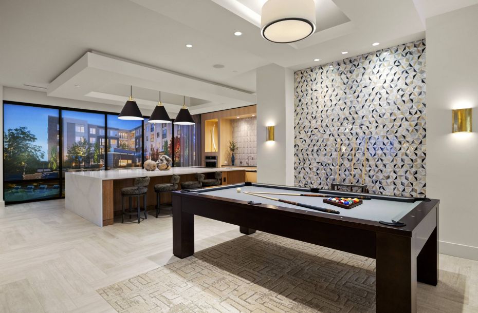 Hanover Company, Hanover Colony Place Luxurious game room with a pool table, bar area, and modern decor. Large windows offer a view of buildings and trees.