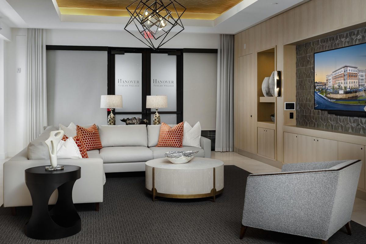 Modern living room with white sofa, patterned pillows, coffee tables, and a wall-mounted TV.