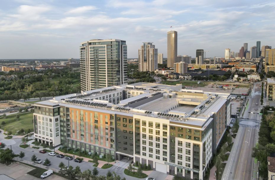 Aerial view of a modern cityscape with a large apartment building and various skyscrapers in the background.