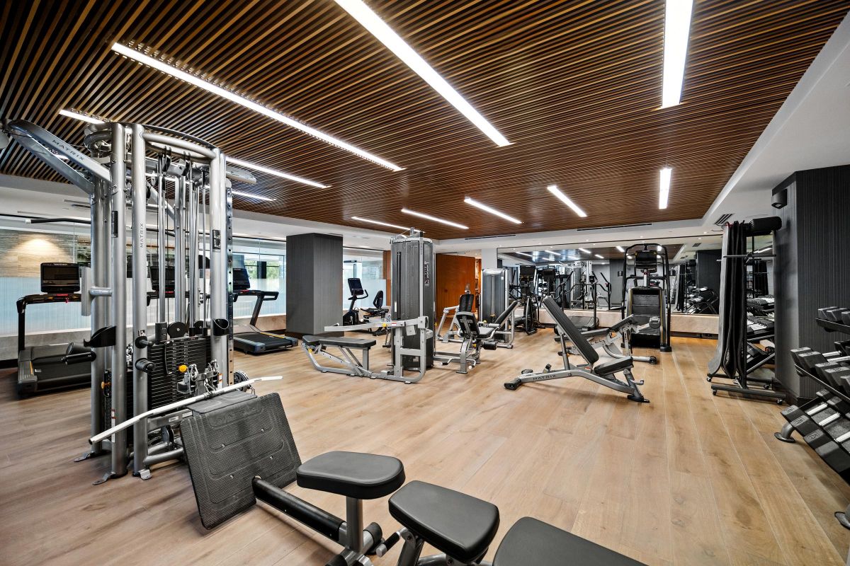 Modern gym with wooden ceiling, mirrors, and various exercise equipment, including weights and machines.