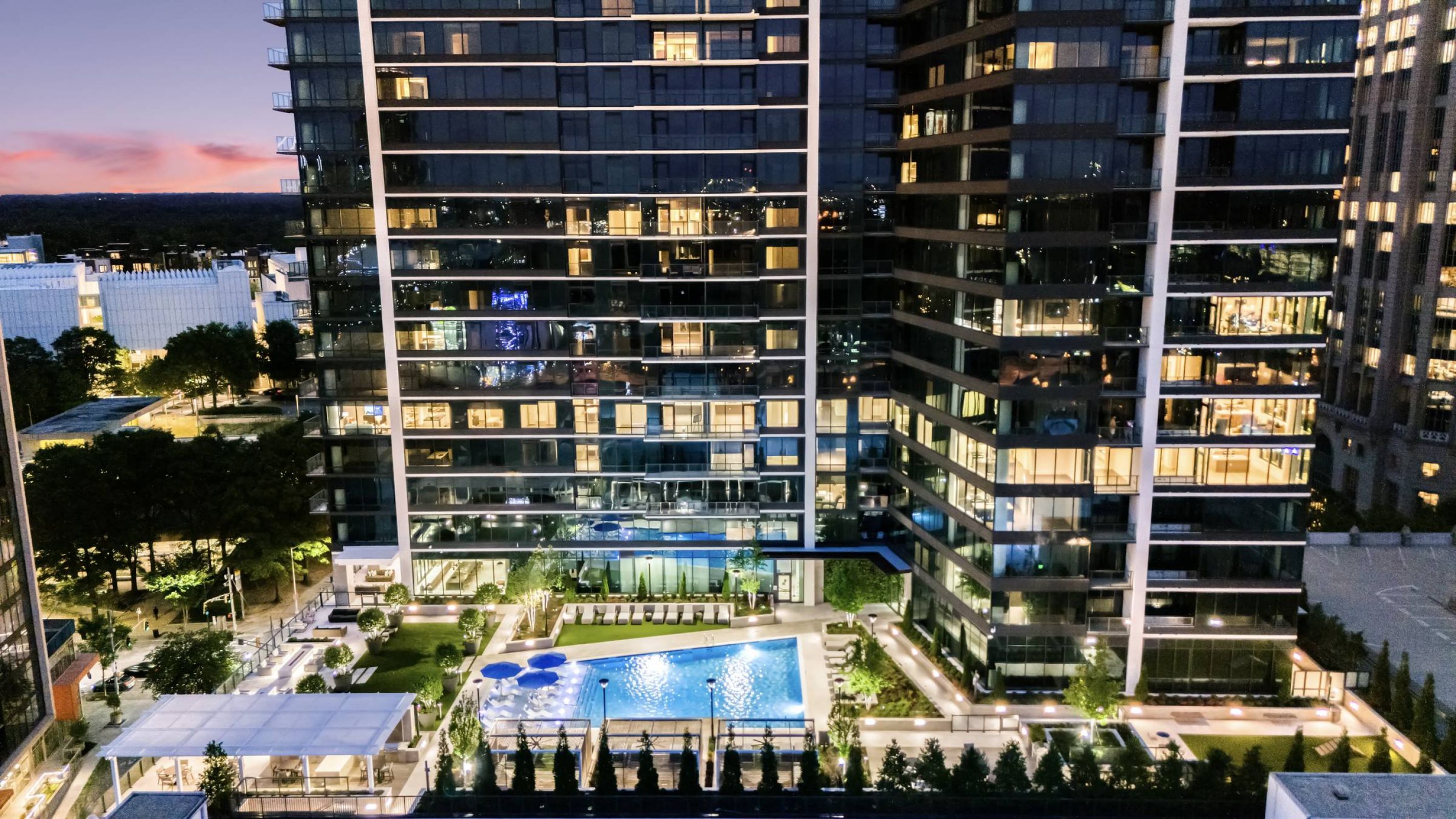 Hanover Company, Hanover Midtown High-rise buildings with a lit outdoor pool area and trees, set against a dusk sky.