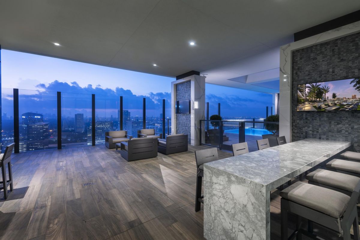 Modern rooftop lounge with city view, featuring seating areas, marble dining table, and night skyline.