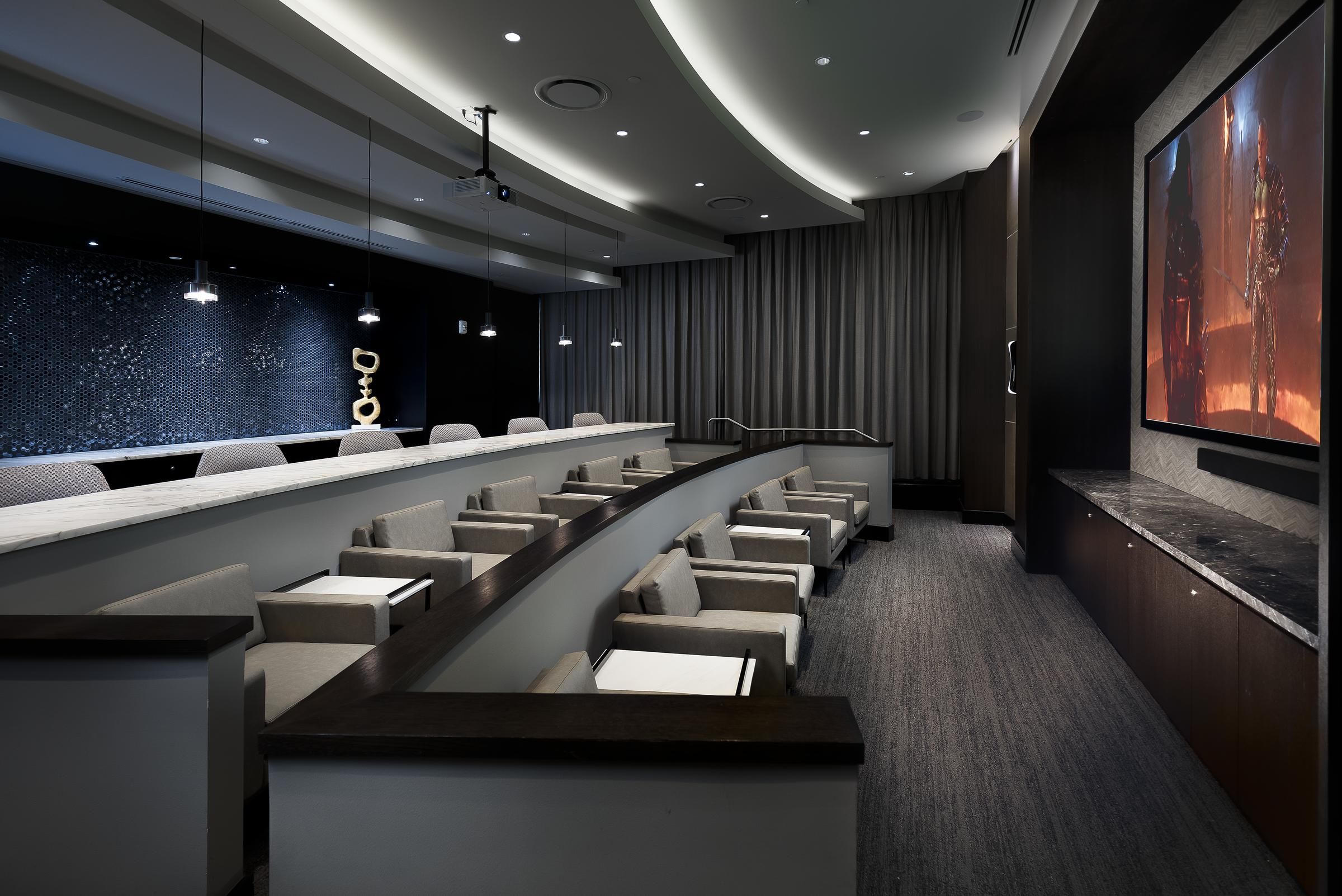 Modern theater room with tiered seating, presentation screen, and decorative wall art at Hanover Driscoll apartments.