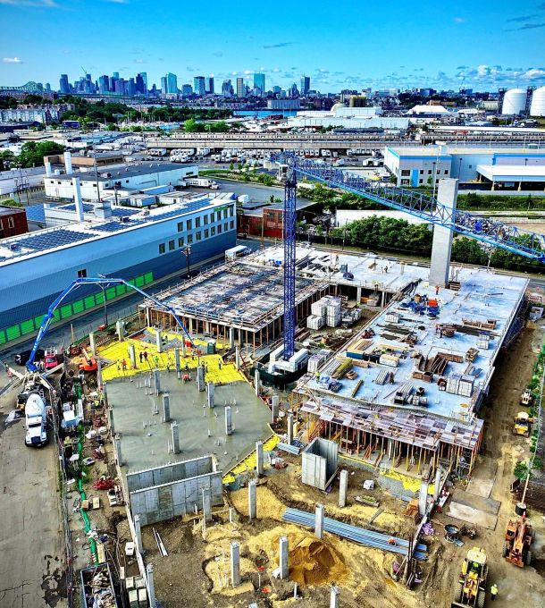 Hanover Company Aerial view of an urban construction site with cranes, buildings, and city skyline in the background under a blue sky.