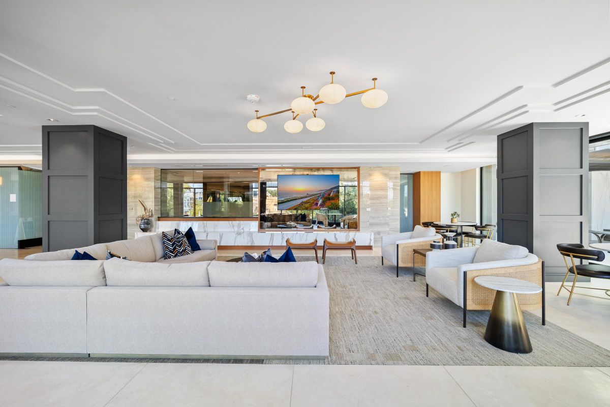 Spacious modern living room with a beige sectional, armchairs, wall-mounted TV, large windows, and contemporary lighting.