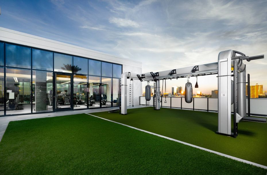 Hanover Company, Hanover River Oaks Rooftop gym with turf and exercise equipment, large glass windows, and a cityscape view at sunset.
