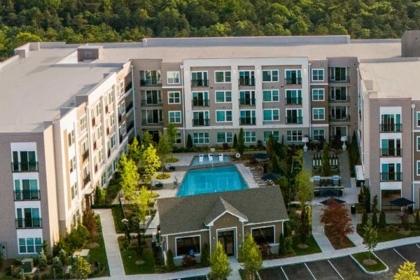 Aerial view of a modern apartment complex with a central swimming pool and surrounding trees.