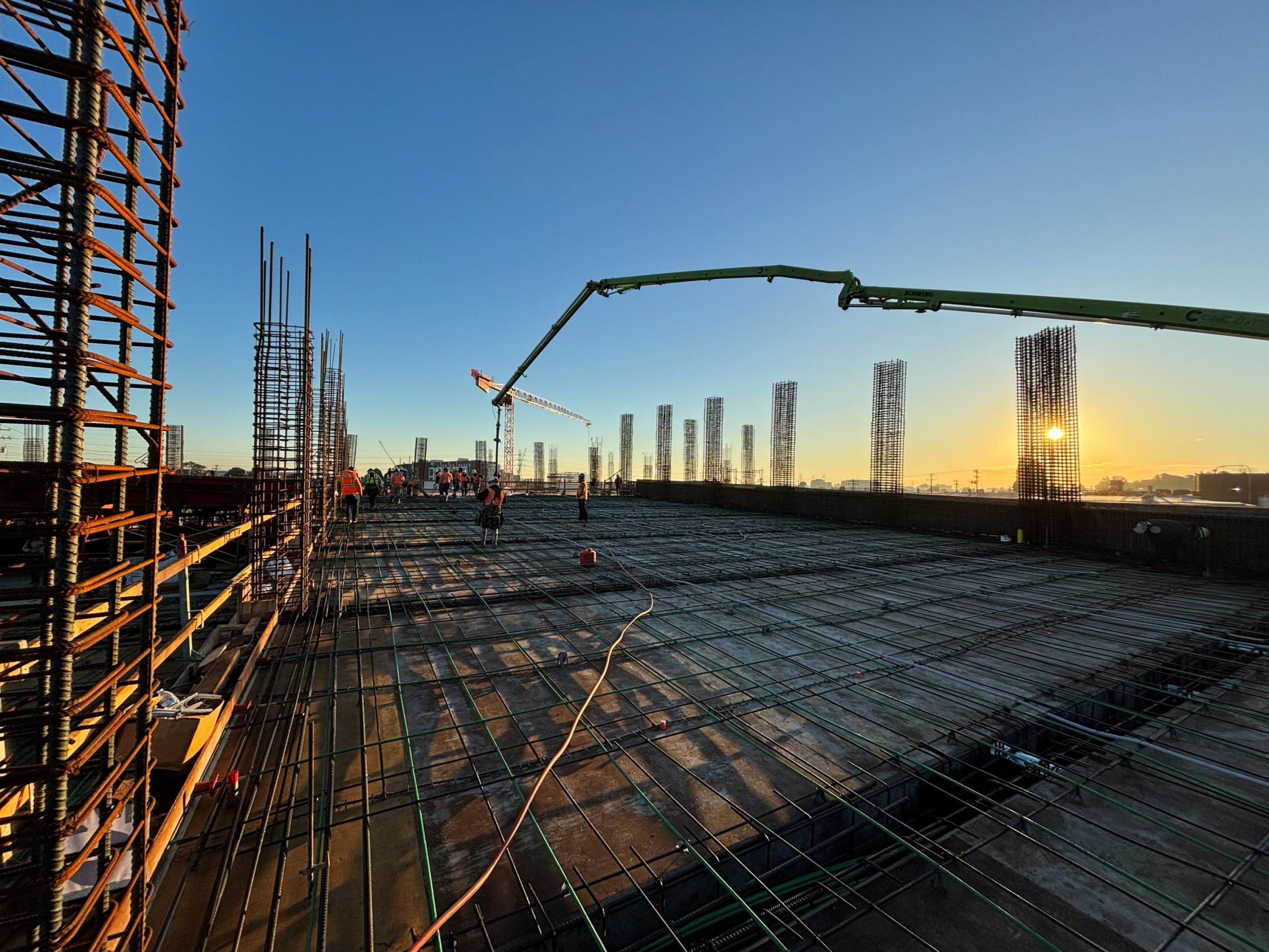 Construction site at sunrise with steel beams, concrete, and cranes at Hanover North Rollins apartments.