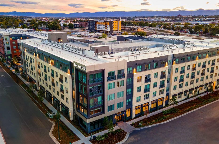 Aerial view of a modern multi-story apartment building with surrounding urban landscape at sunset.