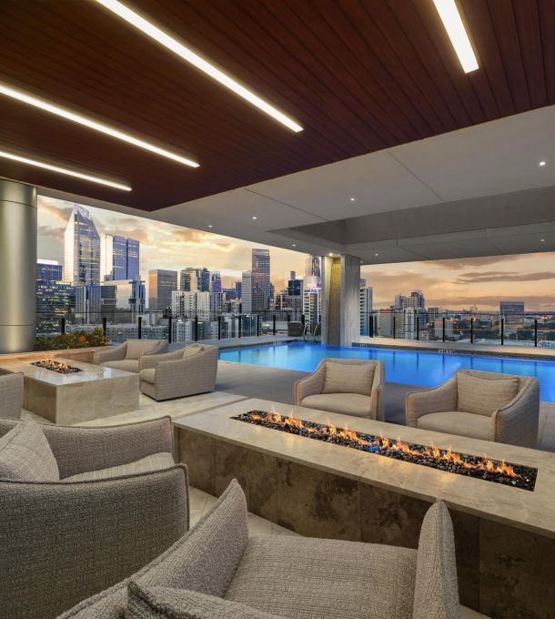 Hanover Company Rooftop lounge with modern decor, fire pits, and a pool overlooking a city skyline at sunset.