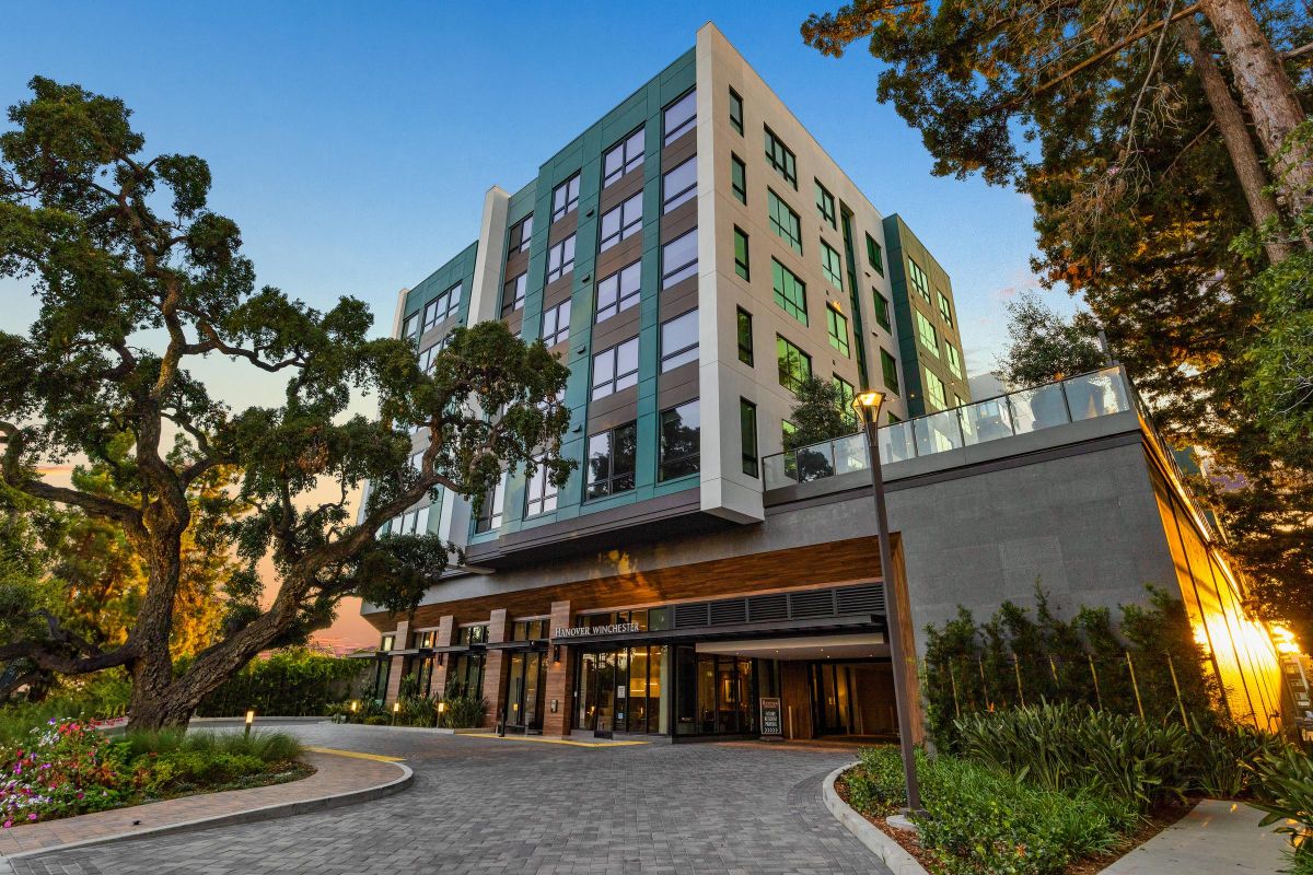 Modern hotel building with large windows, surrounded by trees and landscaping, under a clear blue sky.