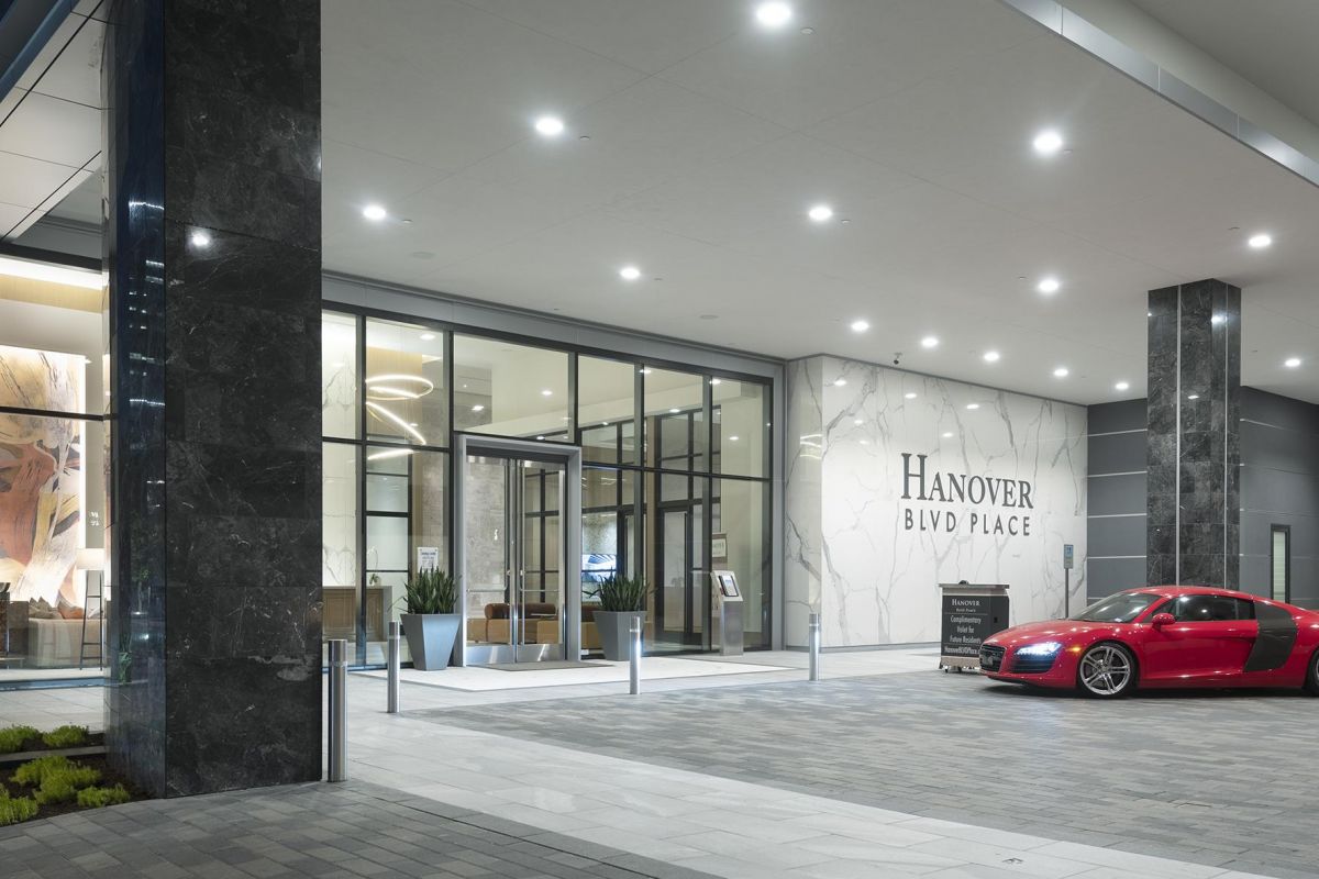 Red sports car parked in front of glass-walled Hanover Blvd Place building with modern lighting.