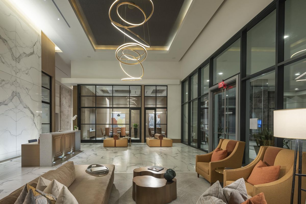 Modern hotel lobby with abstract ceiling lights, marble walls, and beige seating area. Glass wall in the background.