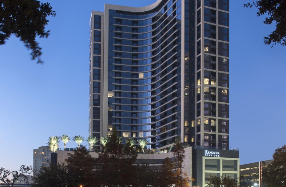 Tall modern hotel building at dusk, with lit windows and palm trees on the rooftop.