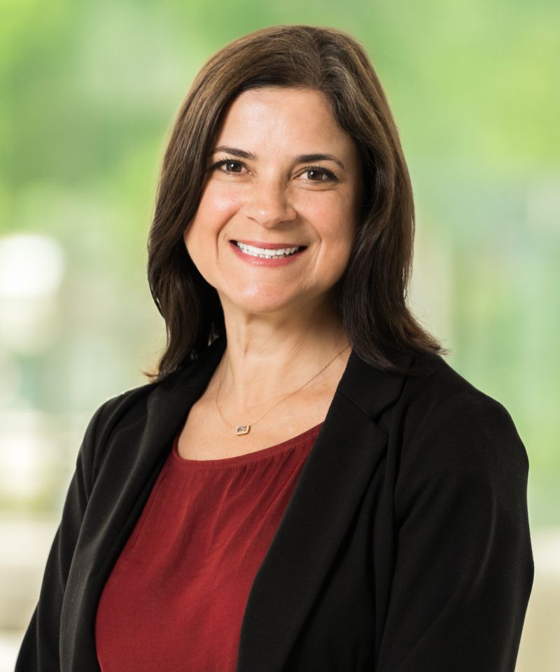 Woman with shoulder-length dark hair wearing a black blazer and red top, smiling at the camera.