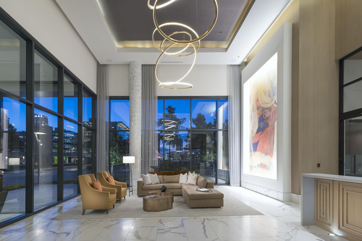 Modern hotel lobby with marble floors, a large artwork, chic seating, and ring-shaped ceiling lights.
