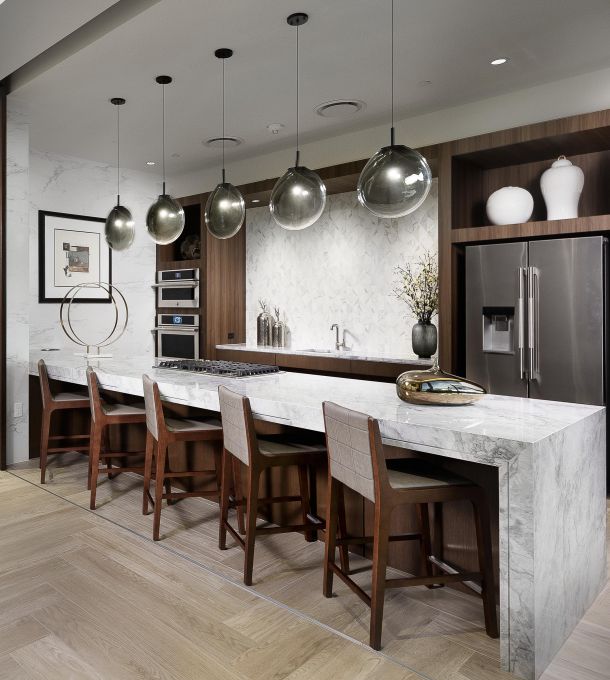 Hanover Company Modern kitchen with marble island, tall chairs, pendant lights, stainless steel appliances, and decorative vases.