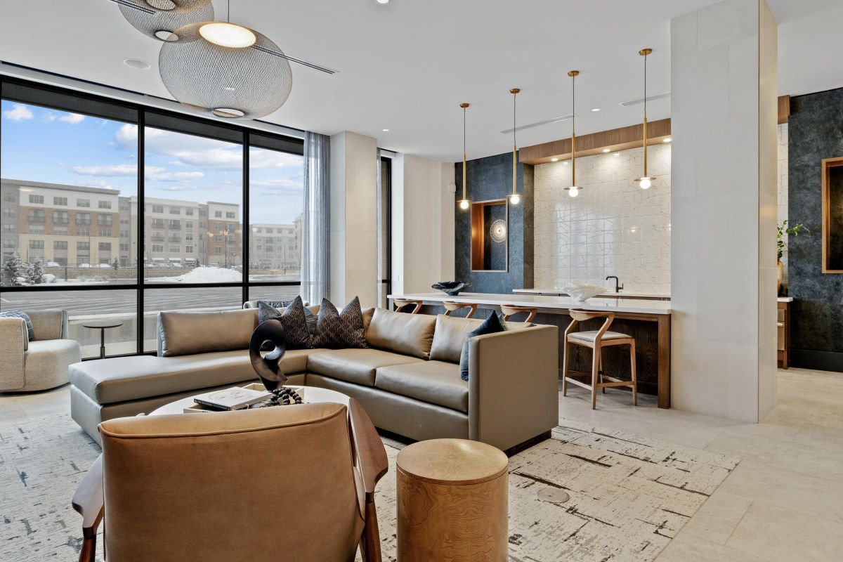 Modern living room with a large sectional sofa, armchair, wooden accents, and pendant lights in front of large windows.