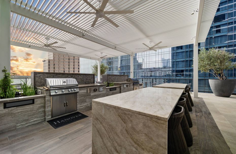Hanover Company, Hanover Brazos Street Rooftop patio with bar seating, modern grill, and ceiling fans, overlooking cityscape at sunset.
